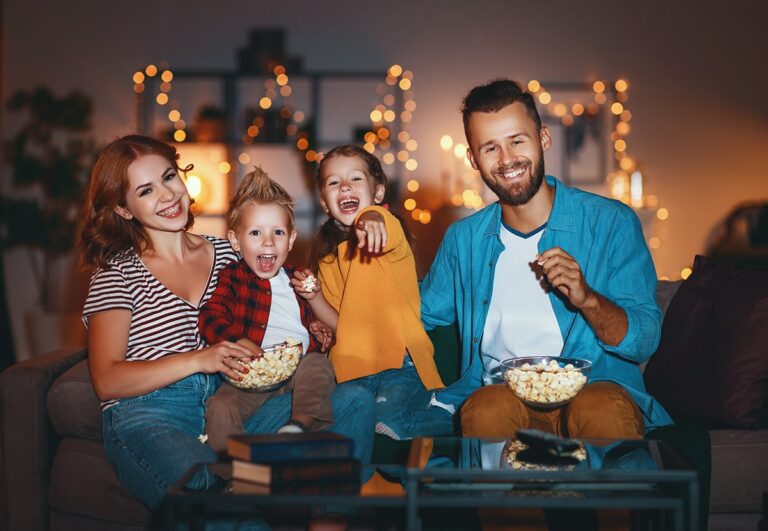 A family of four sits on a couch and watches a movie.