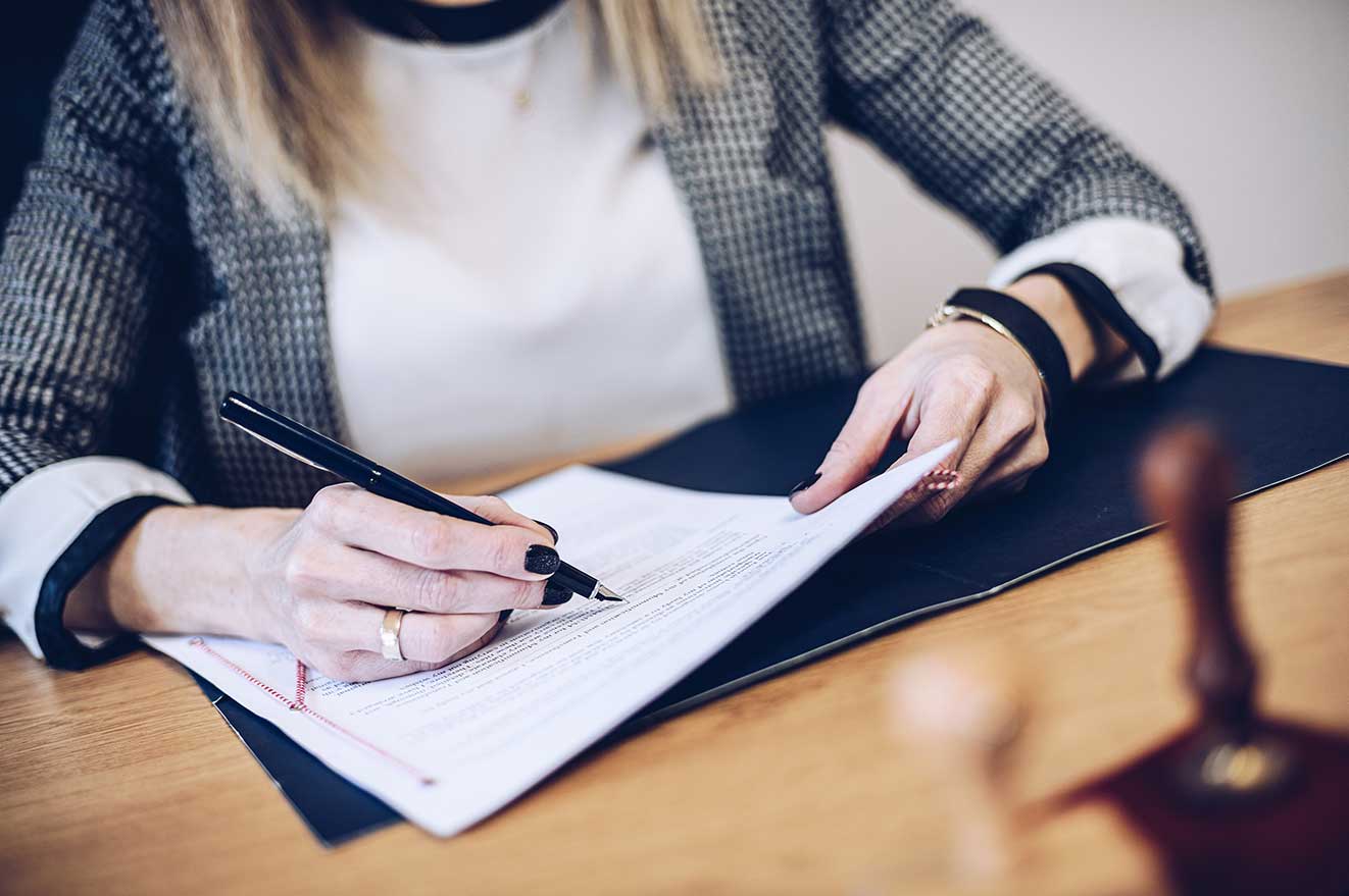 Woman sitting at her desk signing a living trust or other legal document.